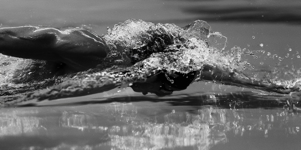 Arm re-entering the water as the head clears the wave, monochrome