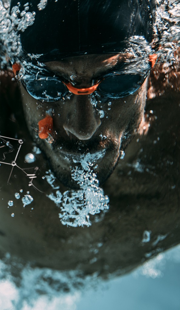 Close underwater view of a swimmer's face and goggles descending through a field of bubbles